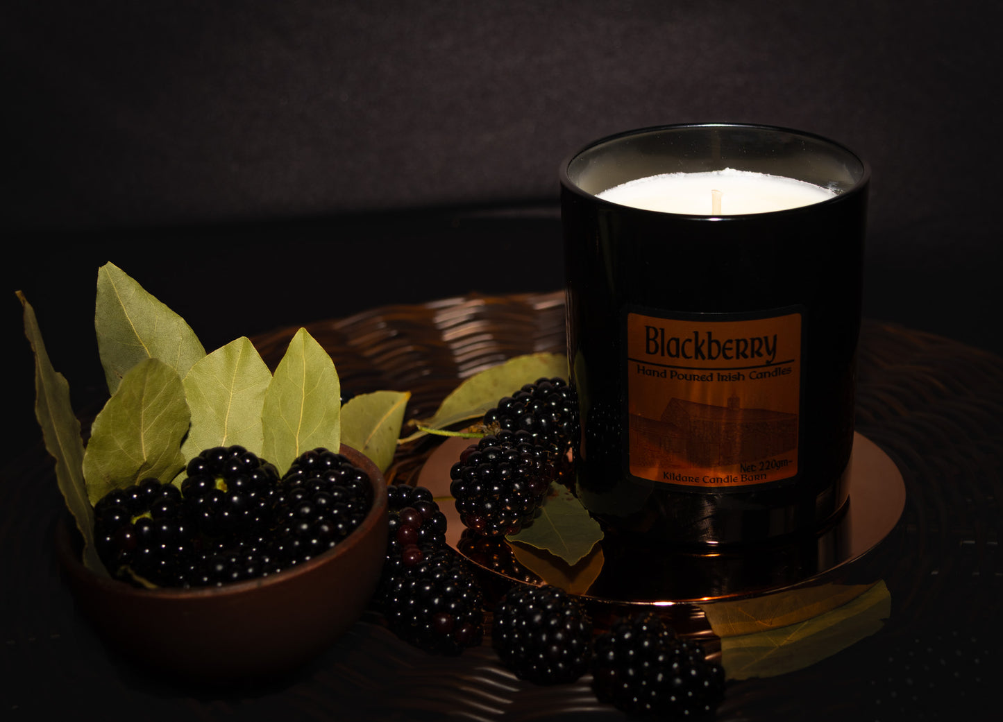 Irish Soy Wax Candle in a black jar with blackberries and bay leaves on a woven surface