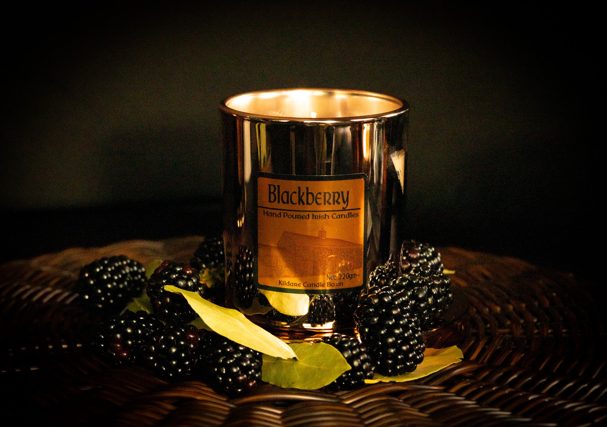 Irish Soy Wax Candle in a copper jar with blackberries and bay leaves on a woven surface