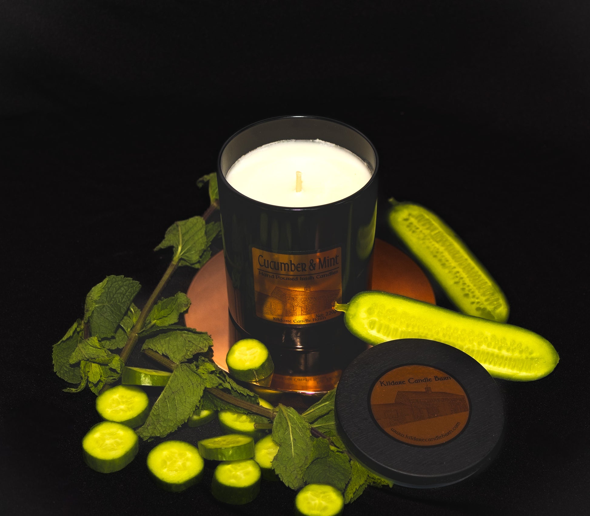 Irish Soy Wax Candle labeled 'Cucumber & Mint' surrounded by sliced cucumbers and mint leaves on a dark background. Black Jar Candle