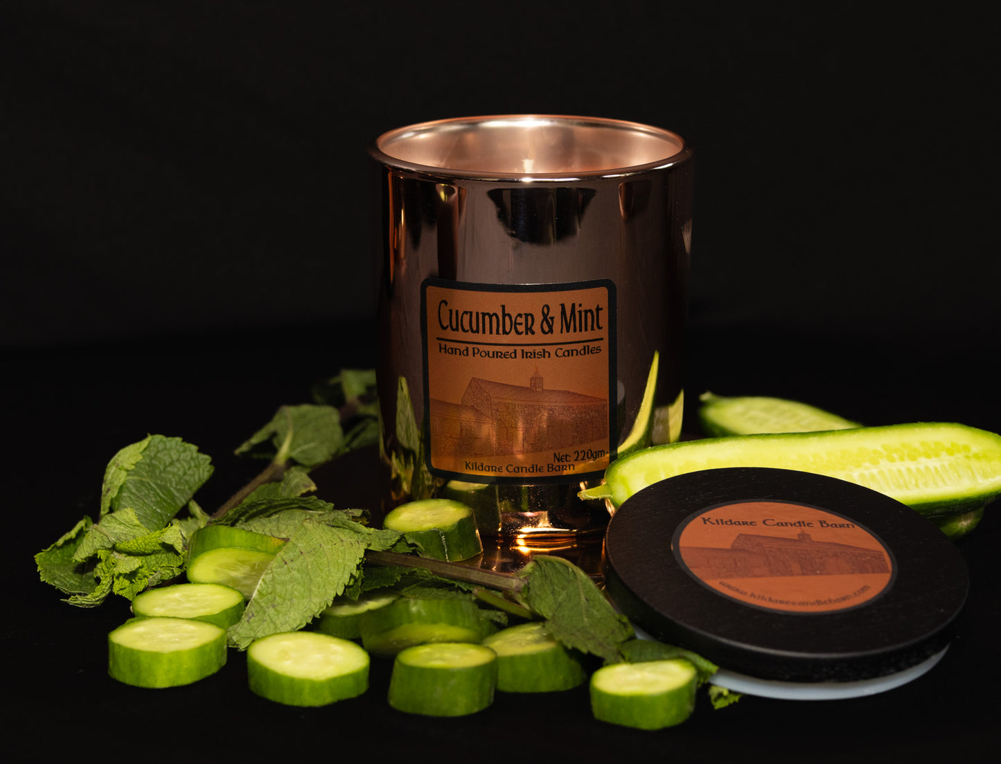 Irish Soy Wax Candle labeled 'Cucumber & Mint' surrounded by sliced cucumbers and mint leaves on a dark background. Copper Jar Candle