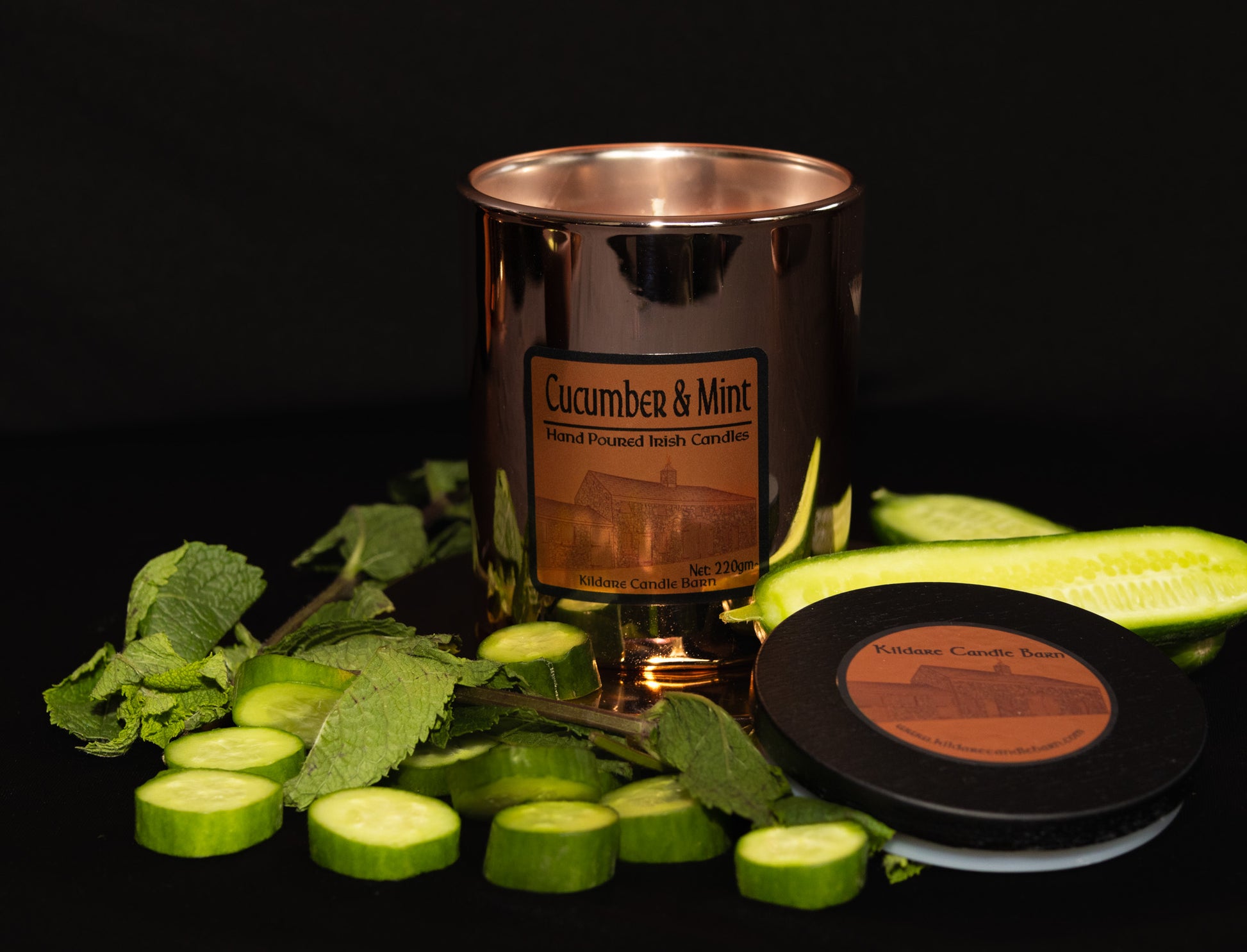 Irish Soy Wax Candle labeled 'Cucumber & Mint' surrounded by sliced cucumbers and mint leaves on a dark background. Copper Jar Candle