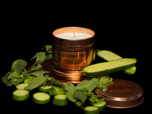 Irish Soy Wax Candle labeled 'Cucumber & Mint' surrounded by sliced cucumbers and mint leaves on a dark background. Copper Tin