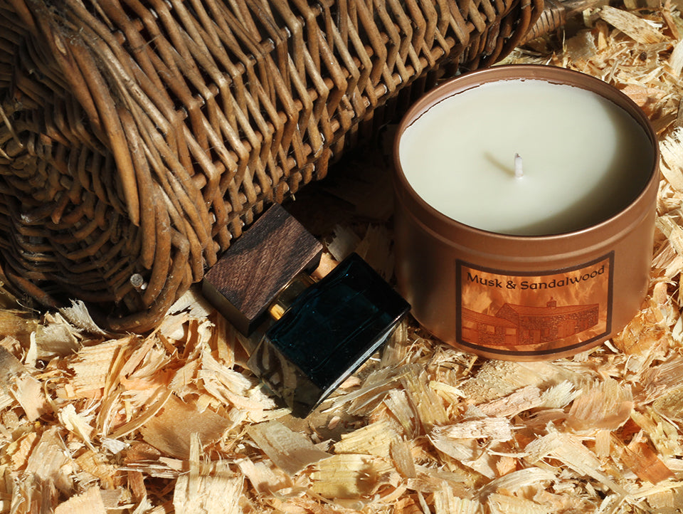 Irish Soy Wax Candle in a copper tin on a bed of wood shavings and bottle of musk cologne