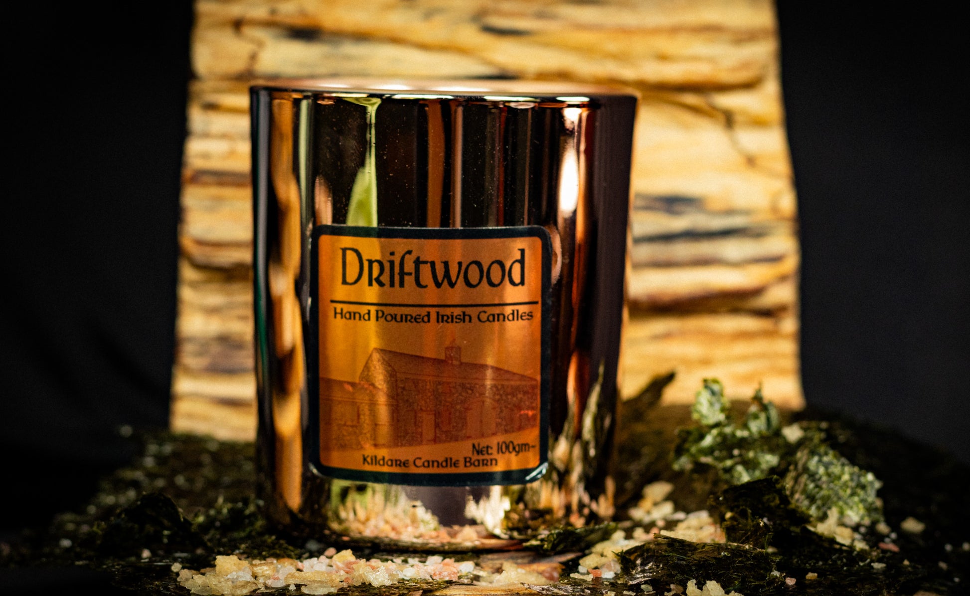 Irish Soy Wax Candle in a 'Driftwood' scented copper jar with a driftwood background and rock salt and seaweed.