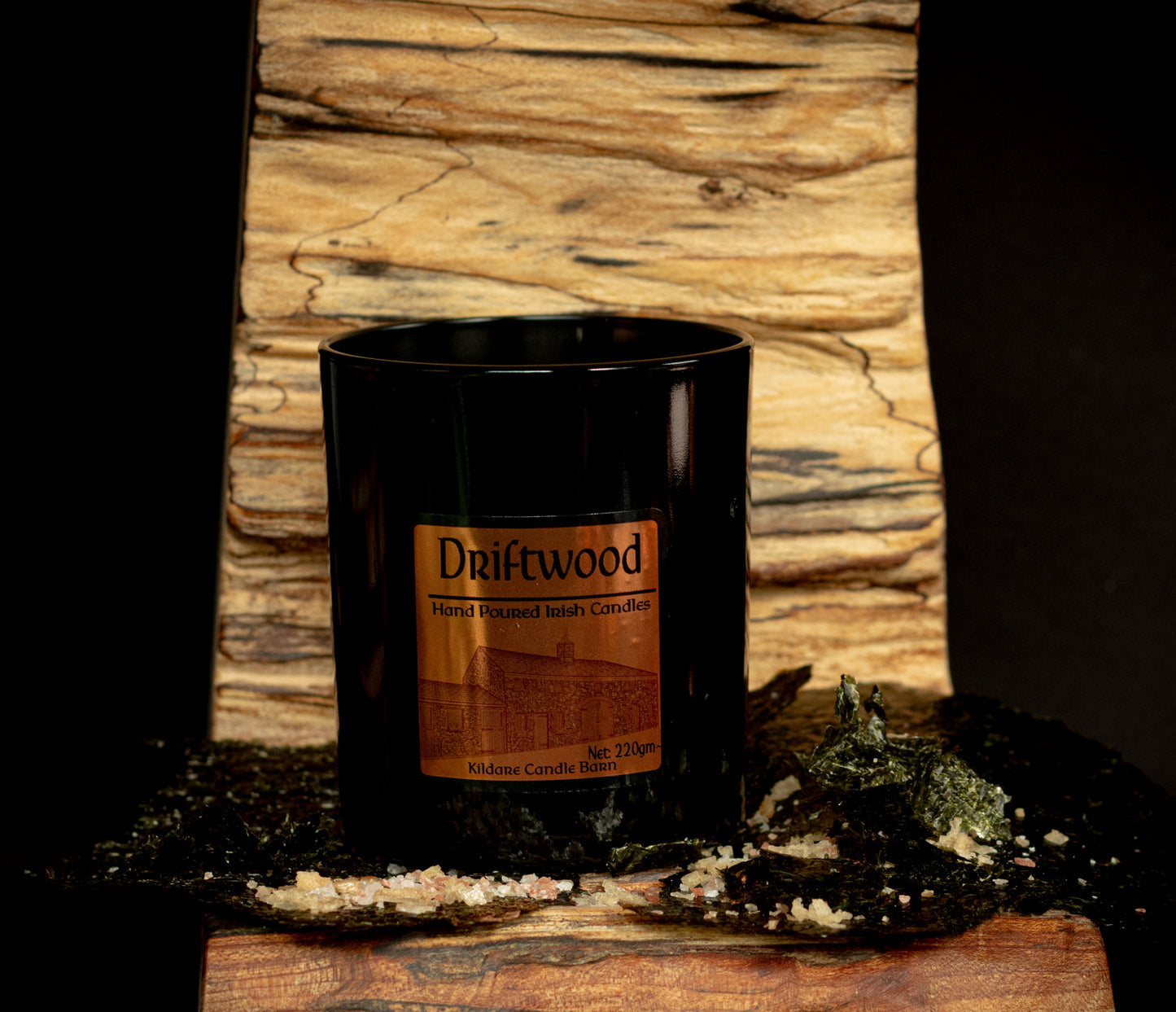 Irish Soy Wax Candle in a 'Driftwood' scented black jar with a driftwood background and rock salt and seaweed.