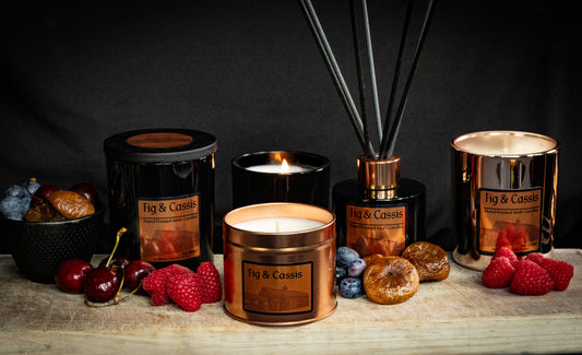 Collection of Fig & Cassis Irish Soy Wax candles and diffusers on a wooden surface with fruits of raspberry, cherry, fig and blueberry