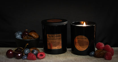 Fig & Cassis Irish Soy Wax candles in a black jar on a wooden surface with fruits of raspberry, cherry, fig and blueberry