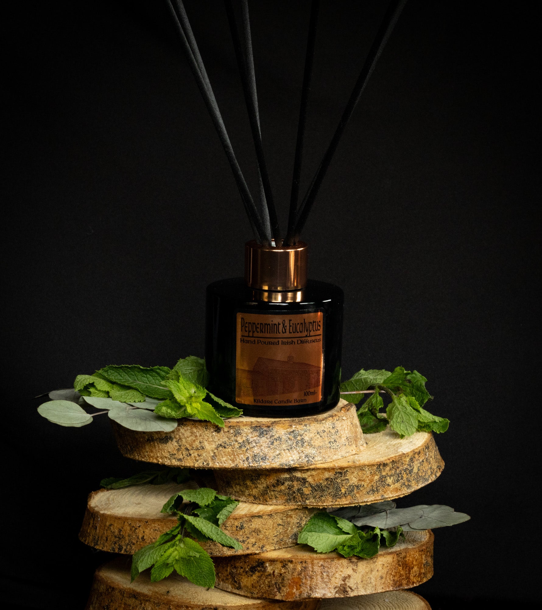 Reed diffuser on a wooden stand with mint & eucalyptus  leaves against a black background