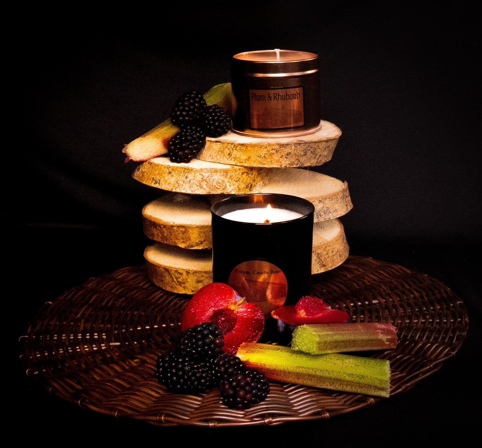 Candle display with various Irish soy wax candles and fruits of plum, rhubarb and blackberry. copper tin and black jar candles.