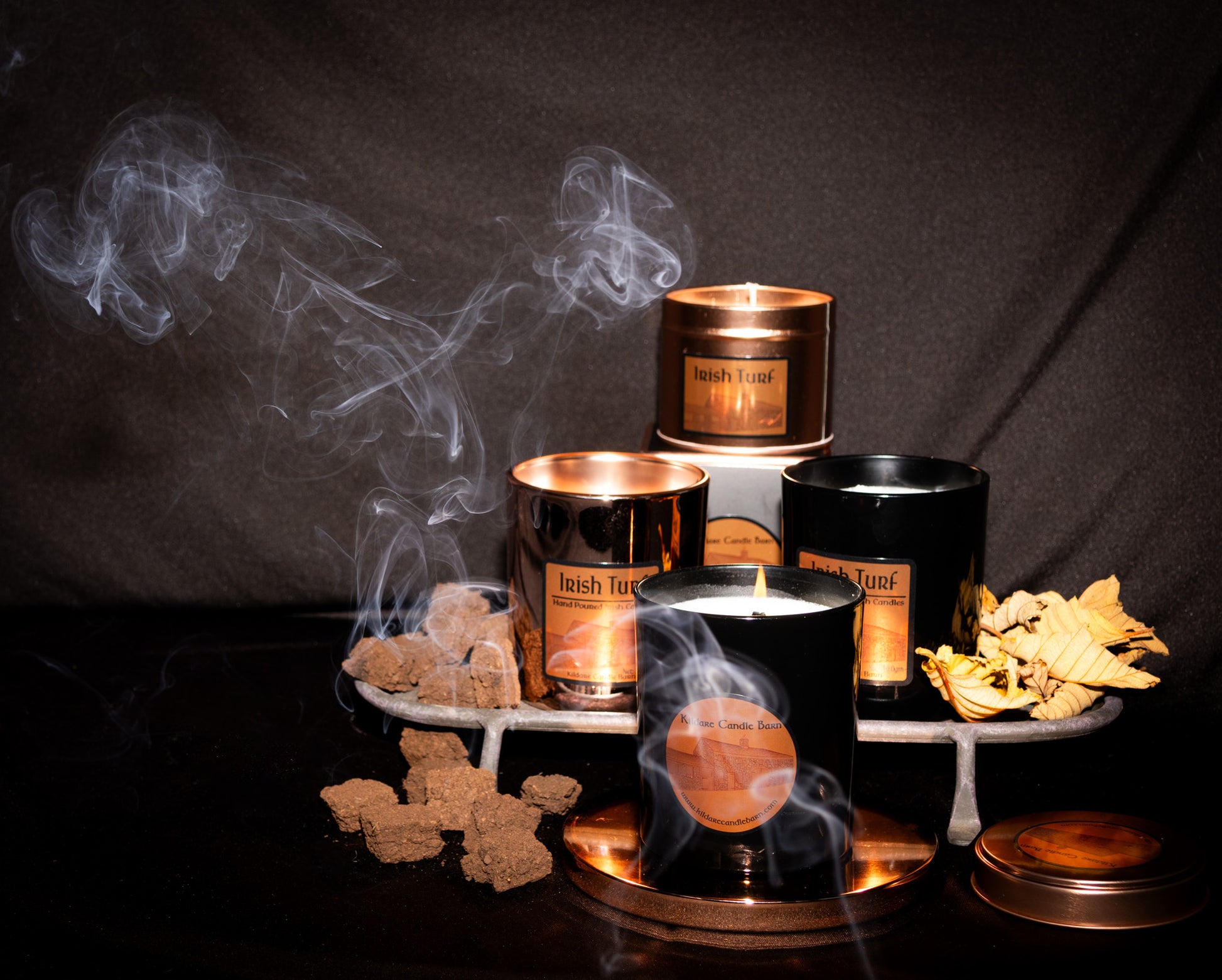 Smoking Irish Soy Wax Candles in  tins and jars with 'Irish Turf' branding on a dark background and  turf pieces