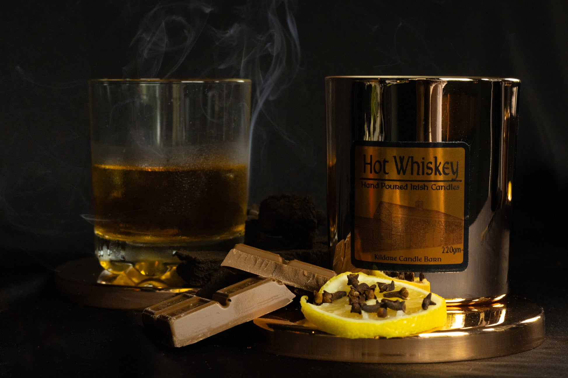 Irish Soy Wax Candle in a Copper Jar with a Hot whiskey glass with a lemon slice and smoking ambiance on a dark background