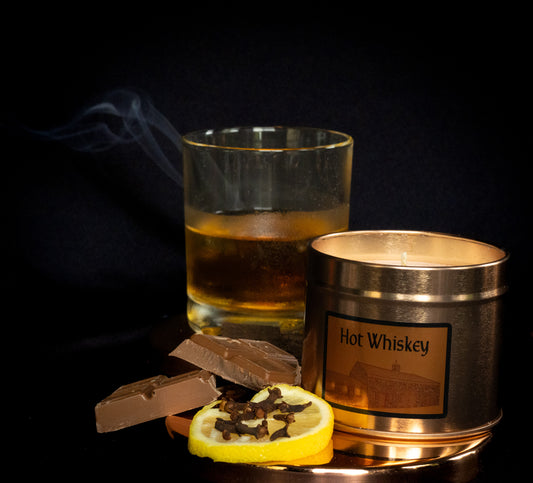 Irish Soy Wax Hot whiskey candle with a glass of whiskey and chocolate and clove studded lemon on a dark background